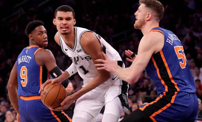 Wembanyama (in white) guarded by RJ Barrett (9) and Isaiah Hartenstein